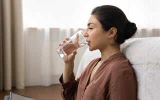 Woman with dry mouth drinking water in bedroom